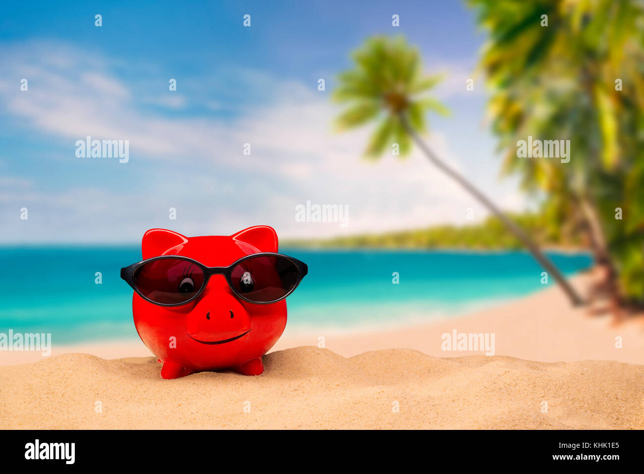 Red piggy bank with sunglasses with a tropical beach in the background Stock Photo