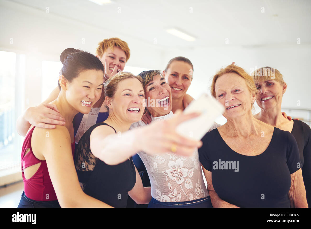 Mixed age group of women laughing while standing together taking selfies during ballet class in a dance studio Stock Photo