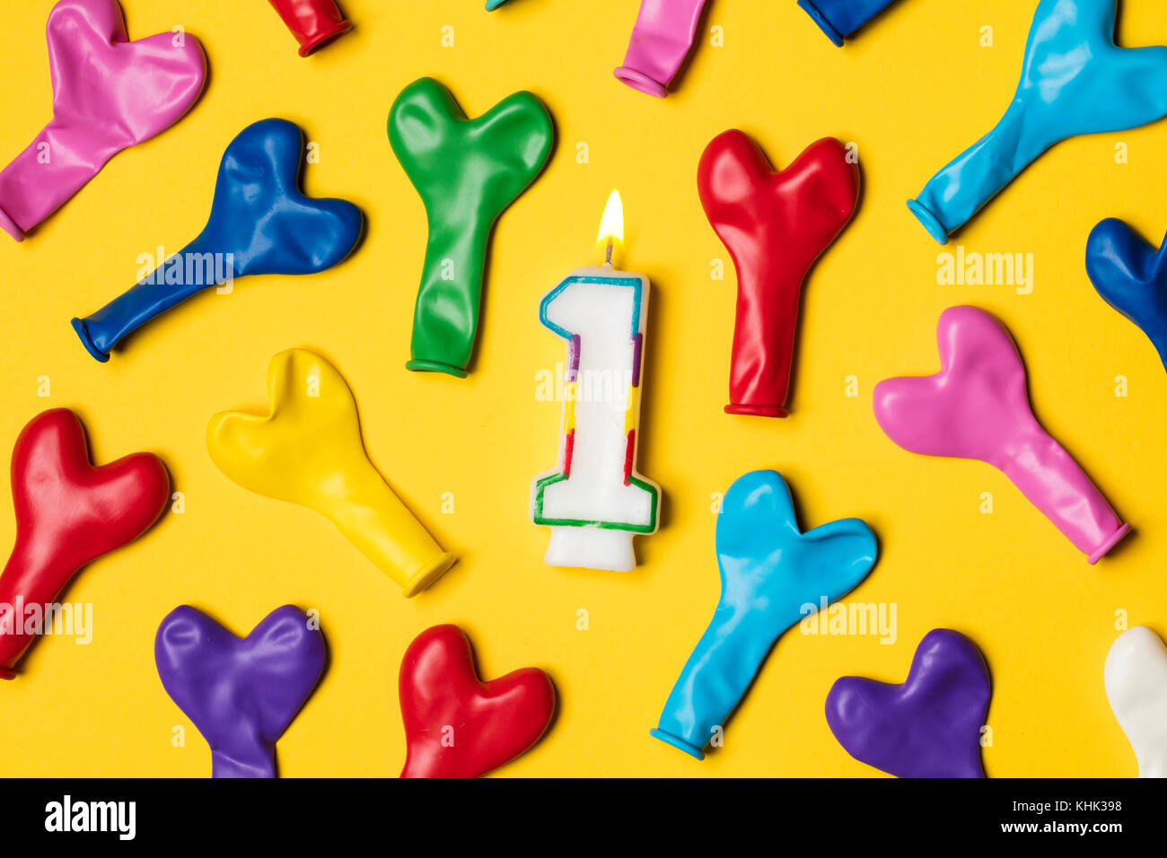Number 1 candle with party balloons on a bright yellow background Stock Photo