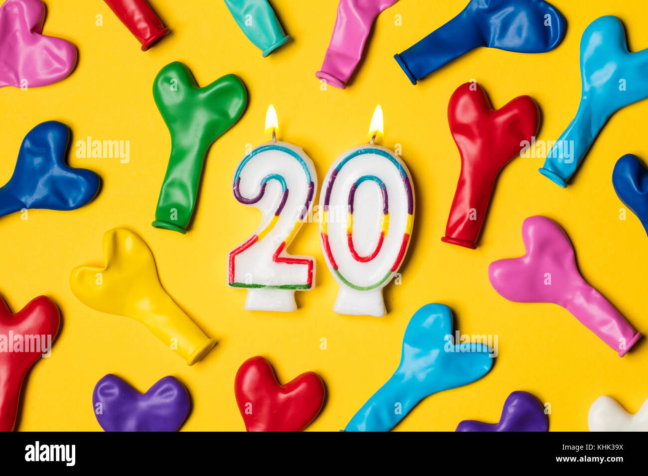 Number 20 candle with party balloons on a bright yellow background Stock Photo