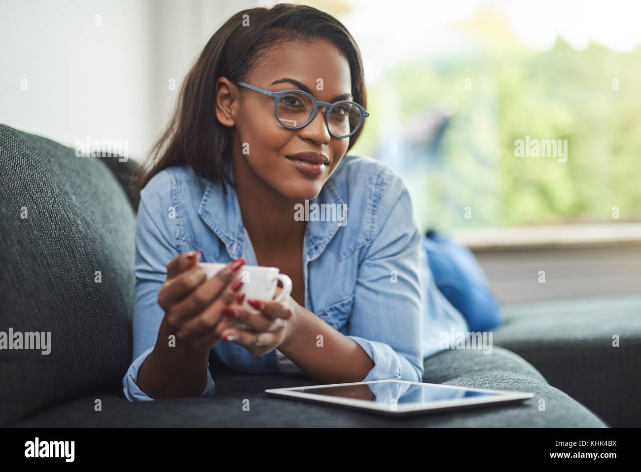 Smiling young African woman wearing glasses lying on the sofa in her ...