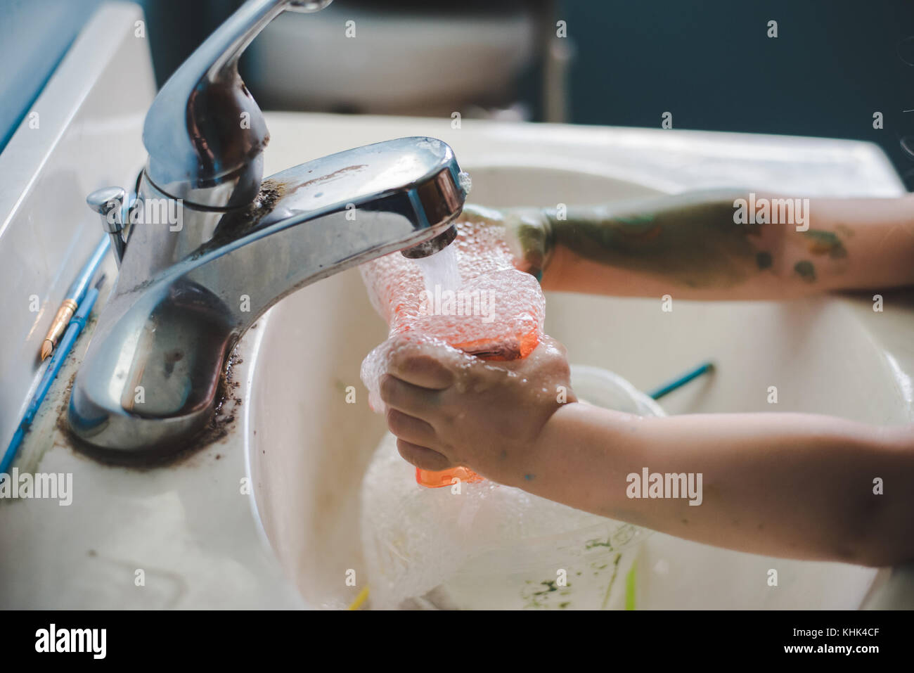 A toddler girl washing paint off her hands in a bathroom sink. Stock Photo