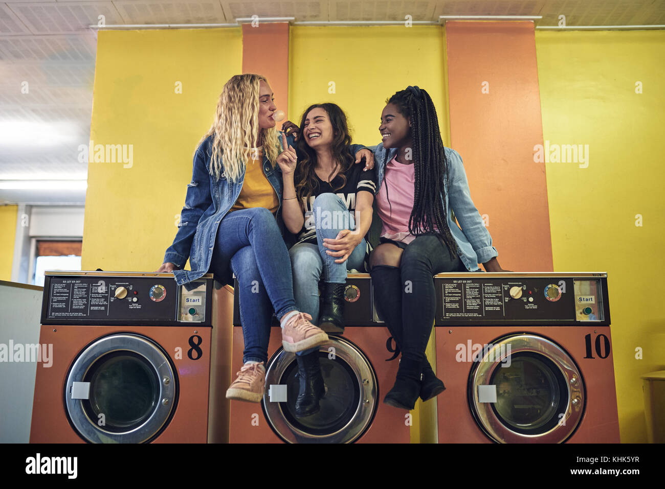 Group of young girlfriends sitting on washing machines in a laundromat