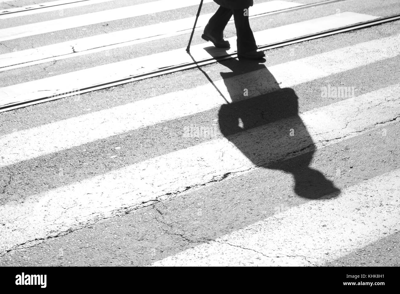 Blurry shadow and silhouette of a senior man crossing the street and zebra crosswalk with  a cane in black and white Stock Photo