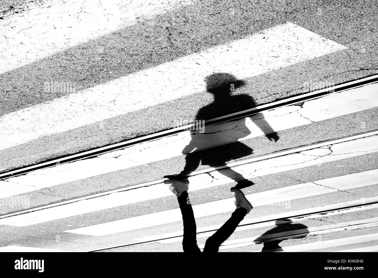 Shadow and silhouette of a teenage girl crossing the street at zebra crosswalk , upside down in black and white Stock Photo