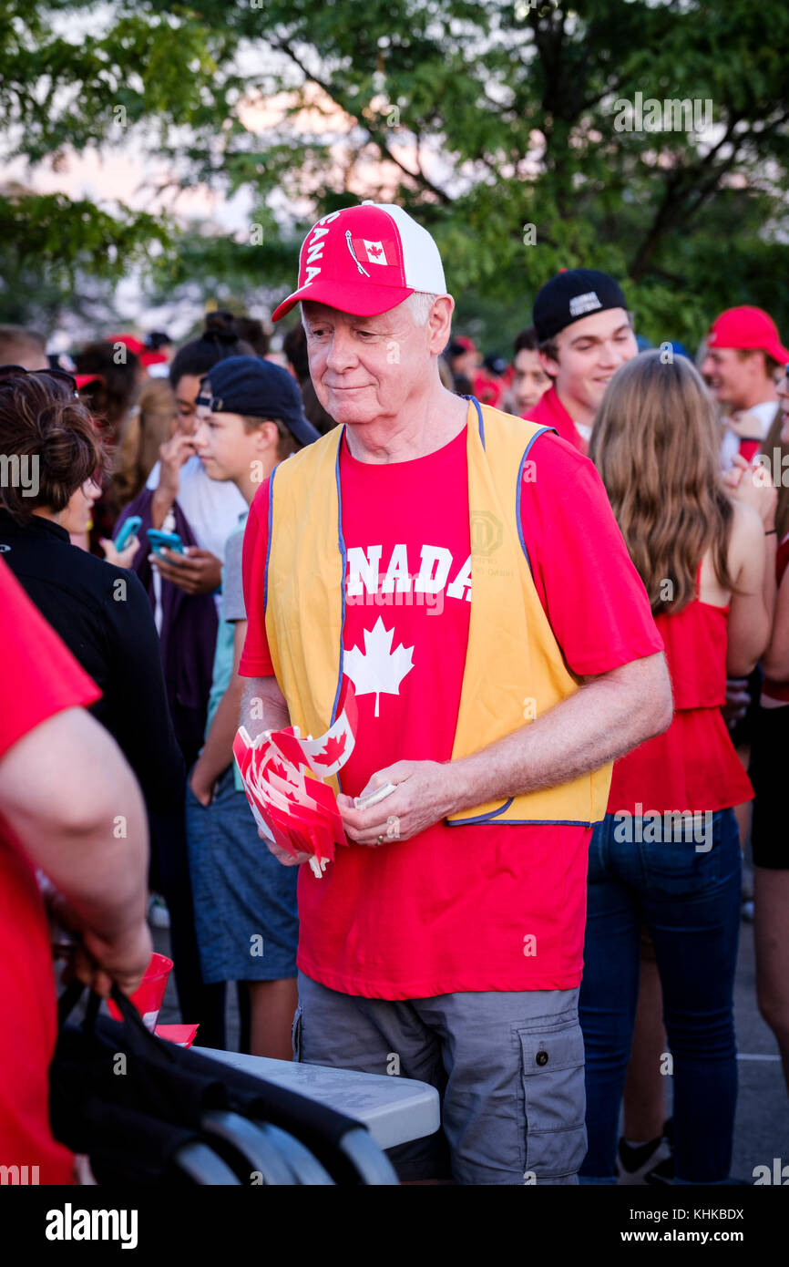 Senior male volunteer distributing Canadian flags during Canada Day celebrations held in London, Ontario, Canada. Stock Photo