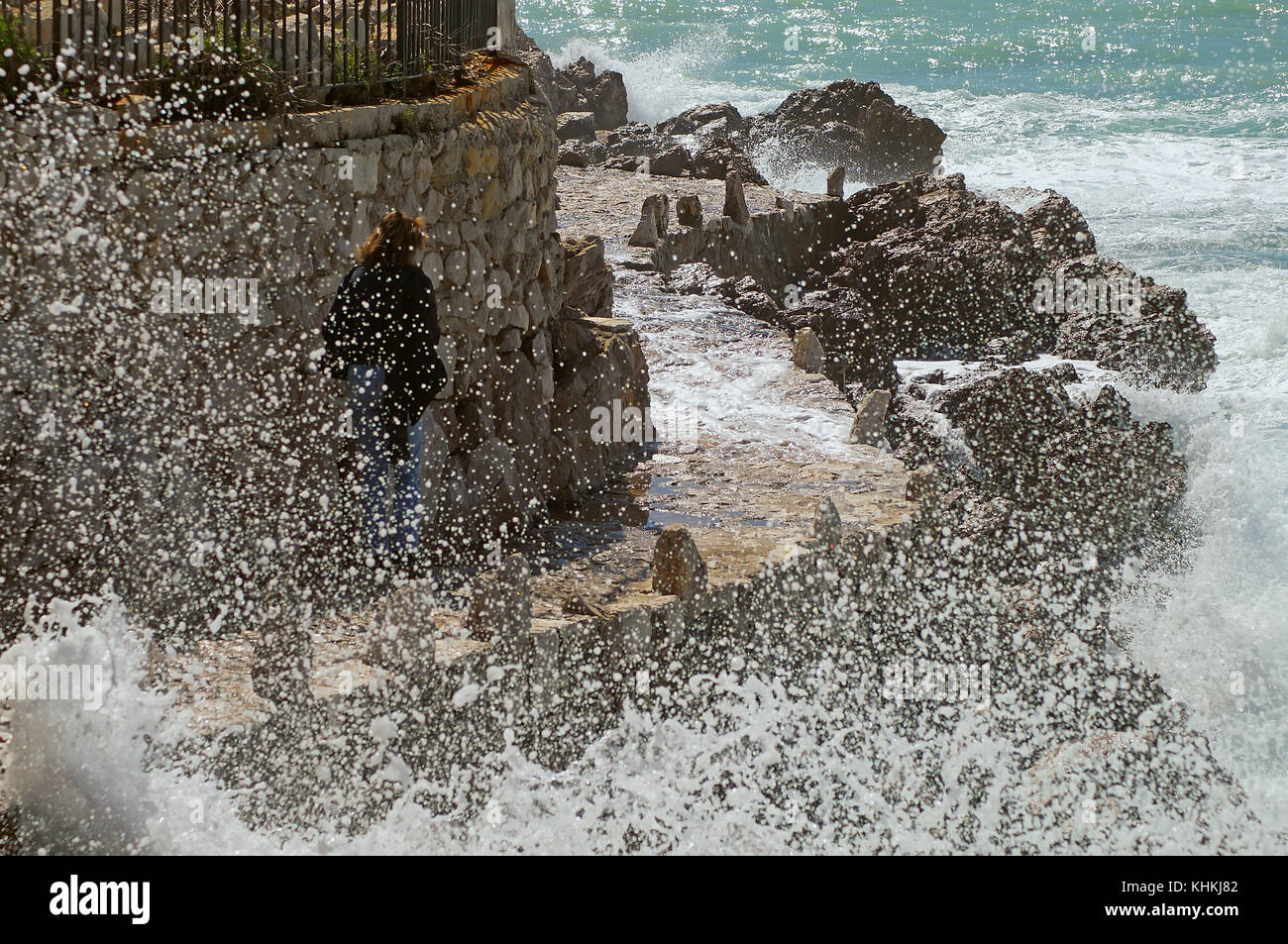 Woman walking on a dangerous path on the coast during a sea storm. Stock Photo