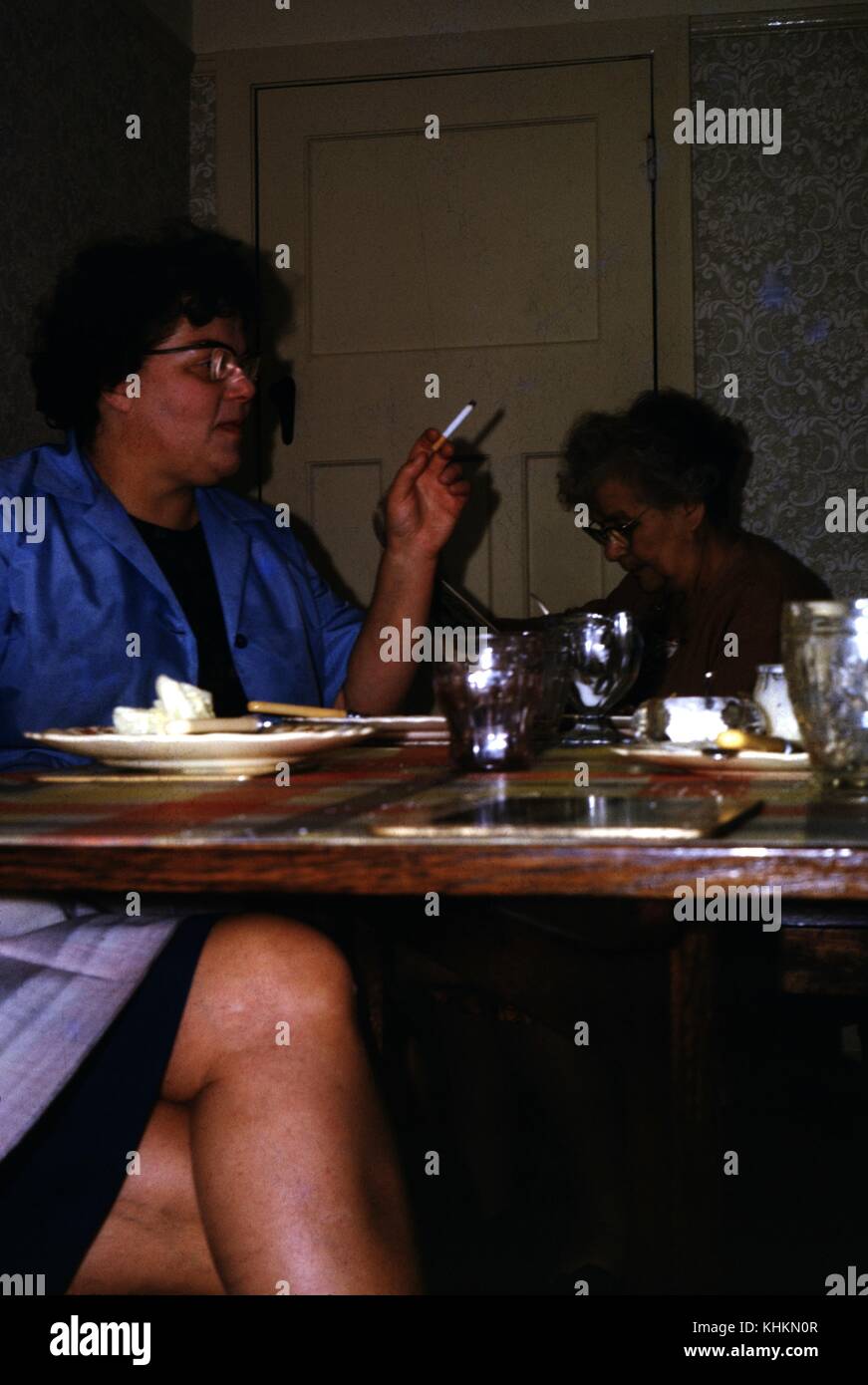 Mature women sitting around a table and smoking cigarettes after having tea, partial view of the underside of the table with a women's legs visible, 1961. Stock Photo