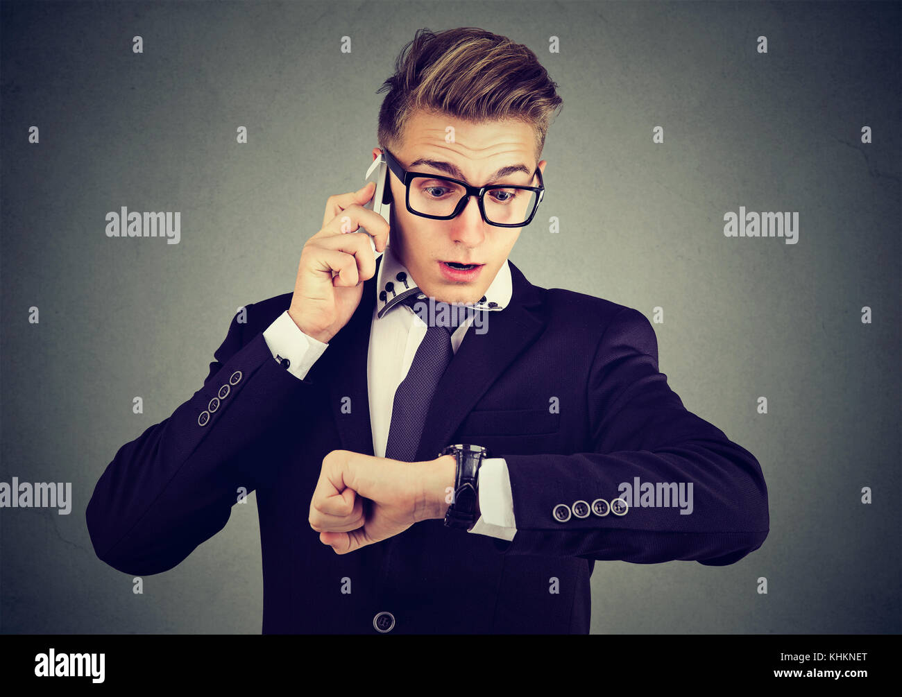 Business and time management concept. Businessman looking at wrist watch, talking on mobile phone running late for meeting. Time is money Stock Photo