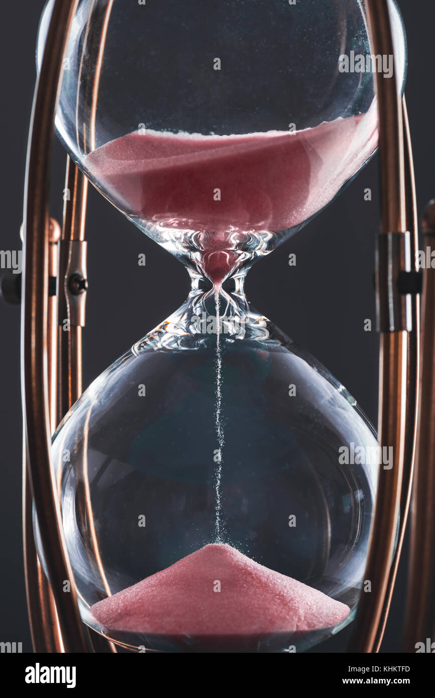 Hourglass with sand in red color and glass body stuck by metal frame. Stock Photo
