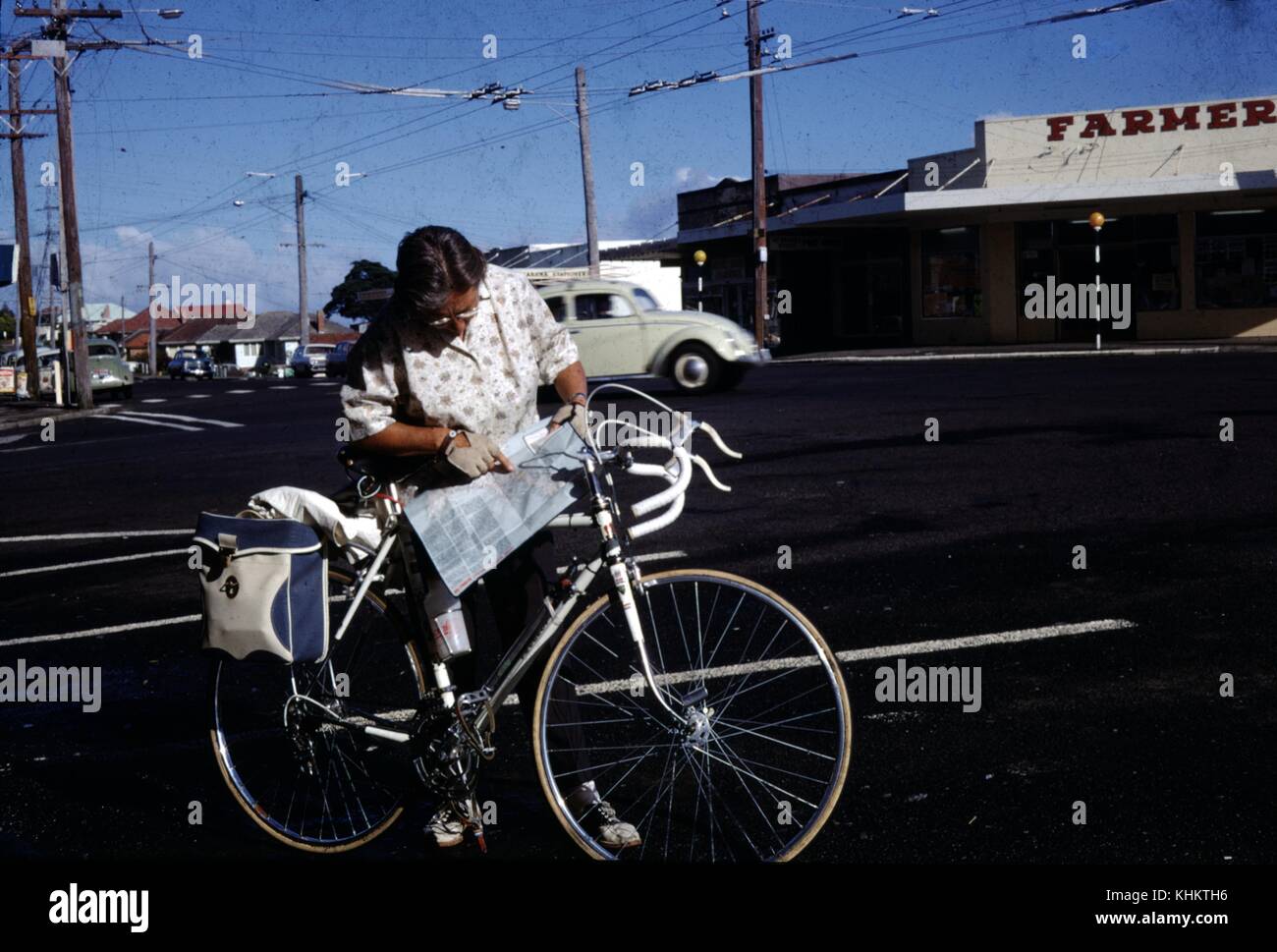 Female tourist with bike stopping in an intersection to examine a map, New Zealand, 1949. Stock Photo