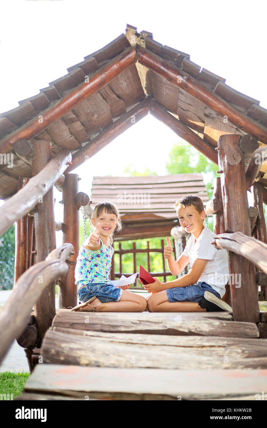 Brother and sister sitting opposite each other in a wooden house at playground with thumps up gesture Stock Photo