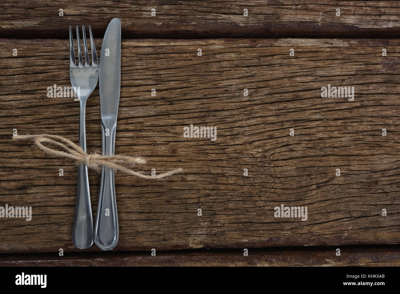 Fork and butter knife tied up with a rope on a wooden table Stock Photo