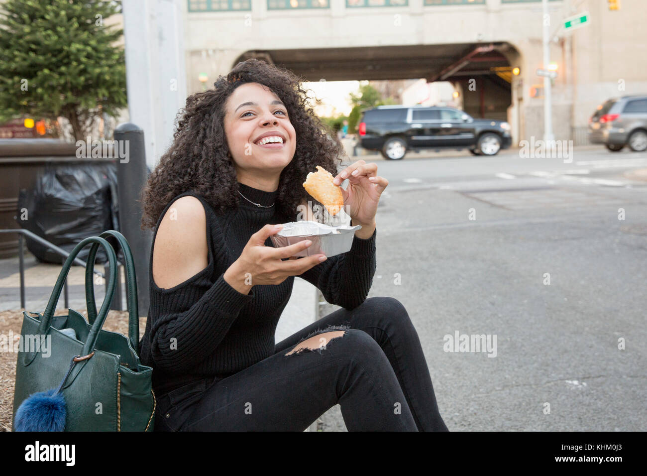 Young woman eating outside a grocery store in Queens, New York Stock Photo