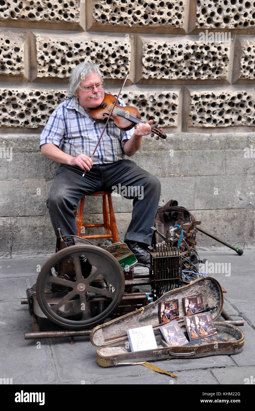 Street busker in Bath plays his violin accompanied by a home made mechanical operated guitar. England,UK Stock Photo