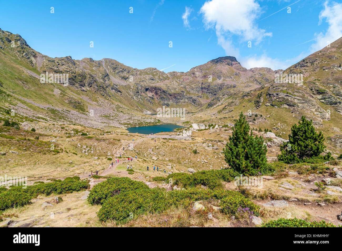 view of high mountain lake called 'Estany del mig' - midle lake,  near Ordino with some people hiking and two mountain pine on the right hand, Tristai Stock Photo