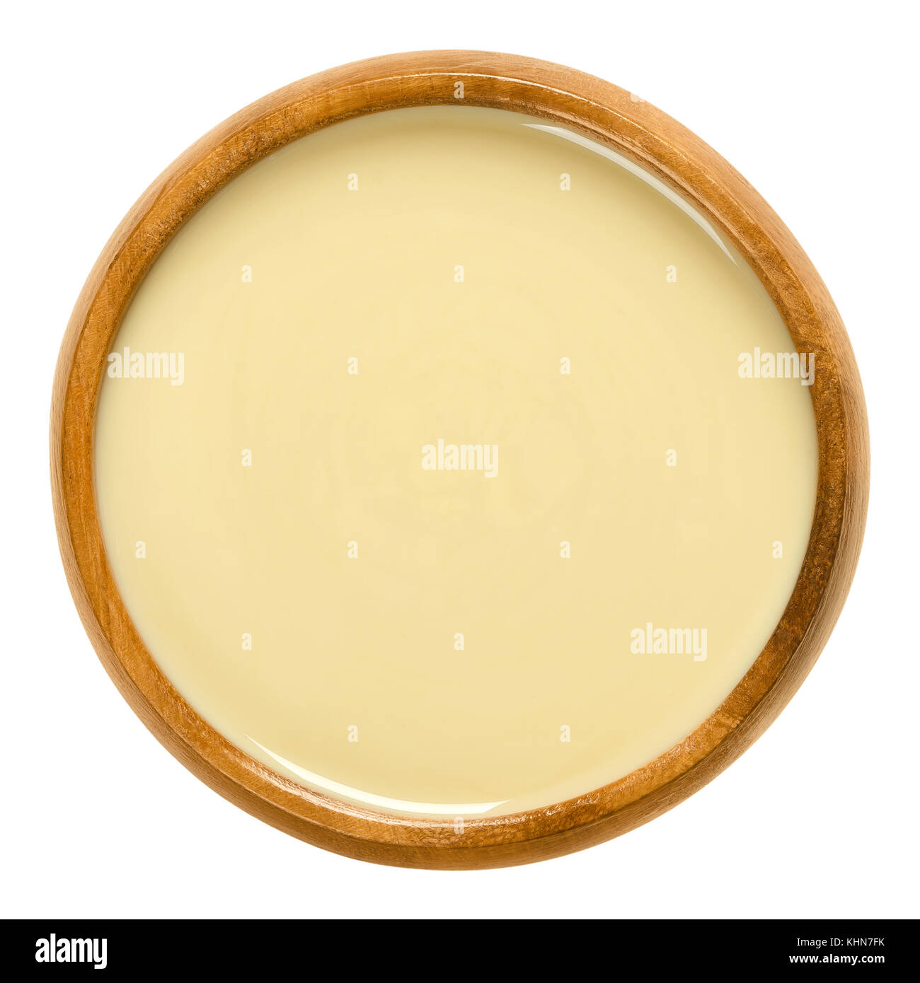 White almond butter in wooden bowl. Smooth food paste made of shelled blanched almonds. Fine puree of the nuts of Prunus dulcis. Isolated macro food p Stock Photo