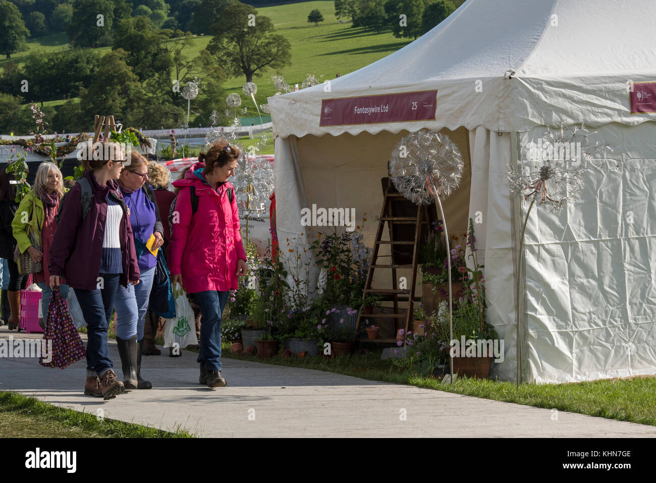 People at showground are walking past a trade stand looking at display of plants & sculptures -  RHS Chatsworth Flower Show, Derbyshire, England, UK. Stock Photo