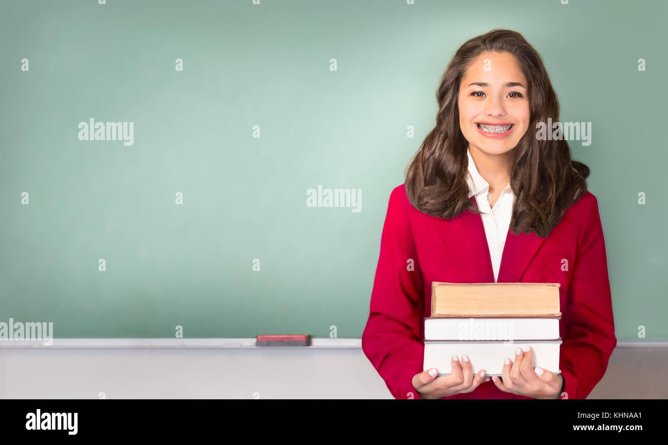 Back to School. Pretty ethnic or Hispanic teen with braces, wearing a red school uniform blazer isolated in front of green chalkboard with Back to sch Stock Photo