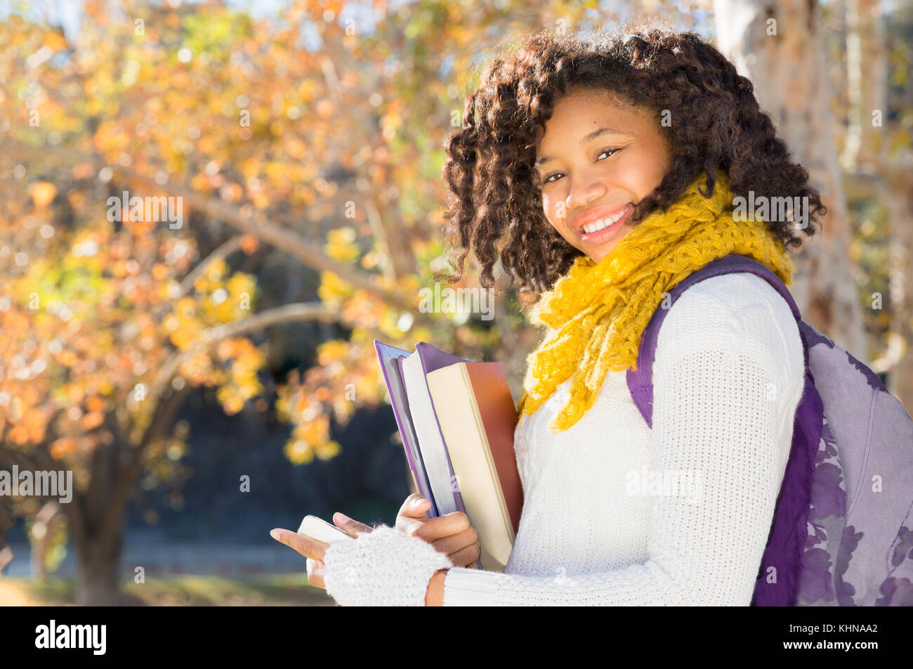 Attractive Black African American Student in Fall with Phone holding books while smiling at camera. Room for copy or text. Stock Photo
