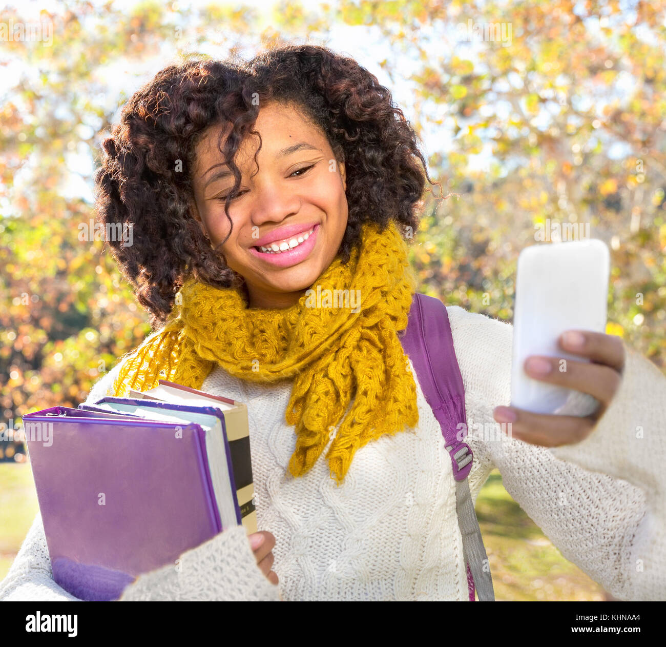 Attractive Black African American Student in Fall with Phone holding books while taking Selfie. Room for copy or text. Stock Photo