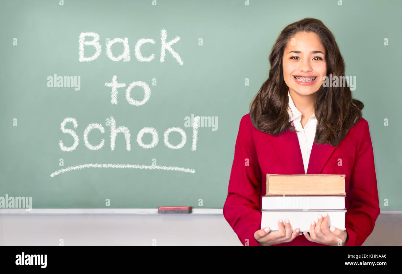 Back to School. Pretty ethnic or Hispanic teen with braces, wearing a red school uniform blazer isolated in front of green chalkboard with Back to sch Stock Photo