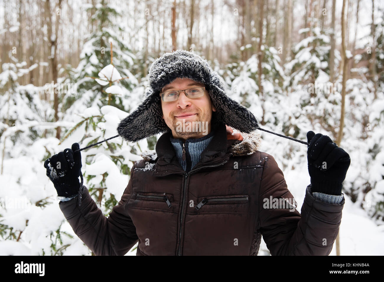 Man in fur winter hat with ear flaps smiling portrait. Extreme in the forest Stock Photo