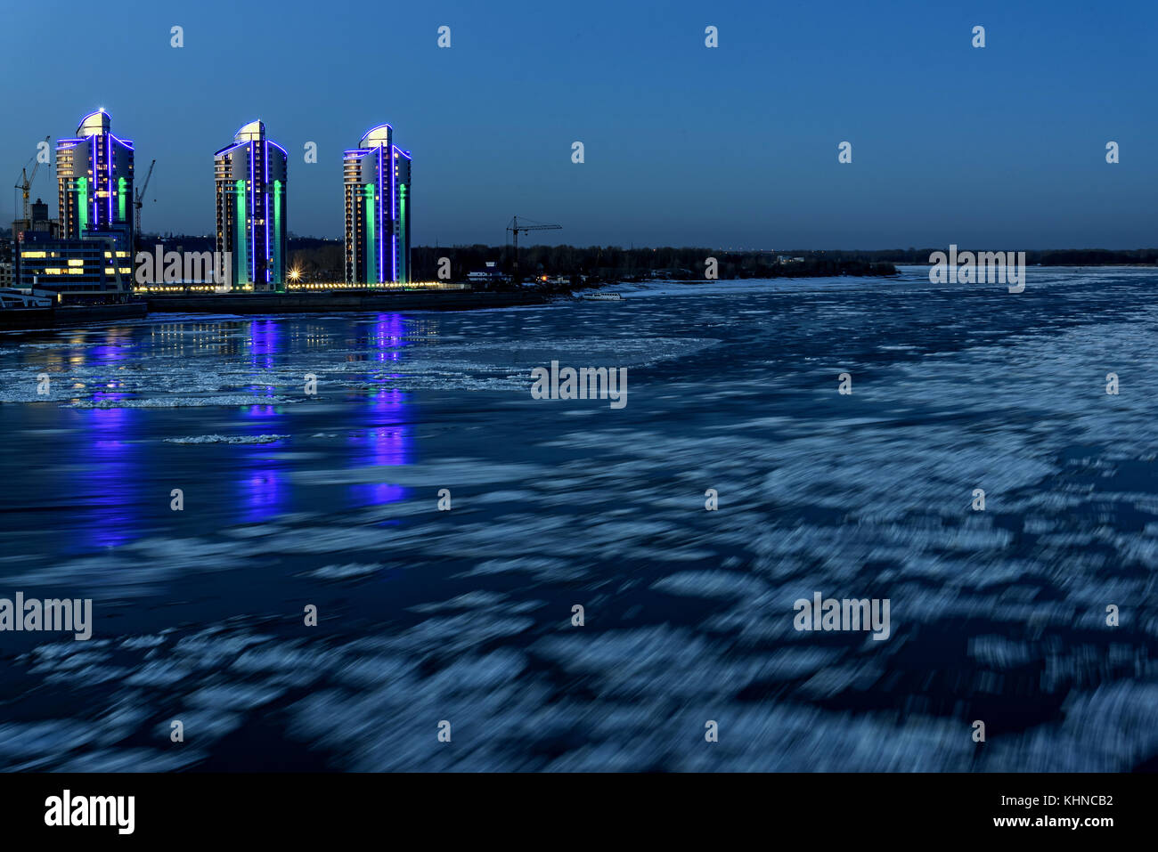 The picturesque night view of the city with lights and river with the reflections of lights in the water and moving ice, shot on a long exposure Stock Photo