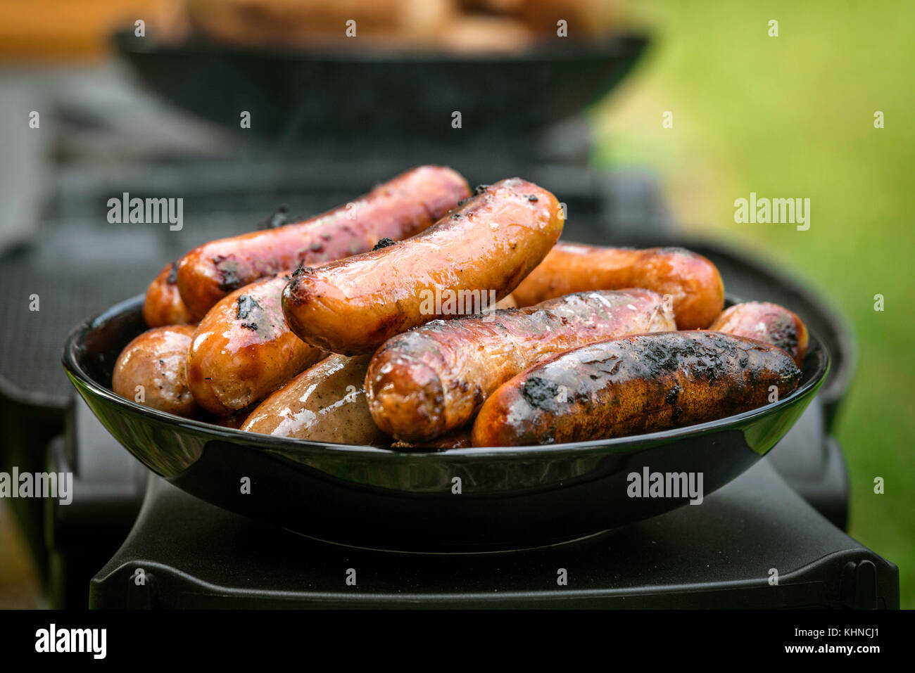 Grilled sausages on a plate at an outdoor barbecue kitchen with a stack of wieners Stock Photo