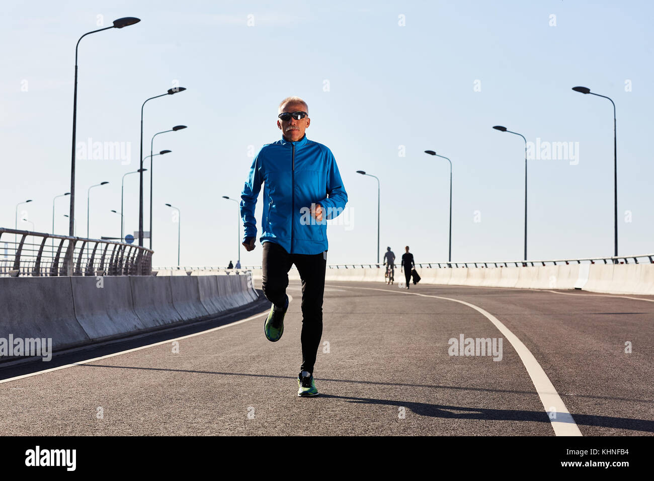 Active mature runner jogging down roadway for sport activities Stock Photo