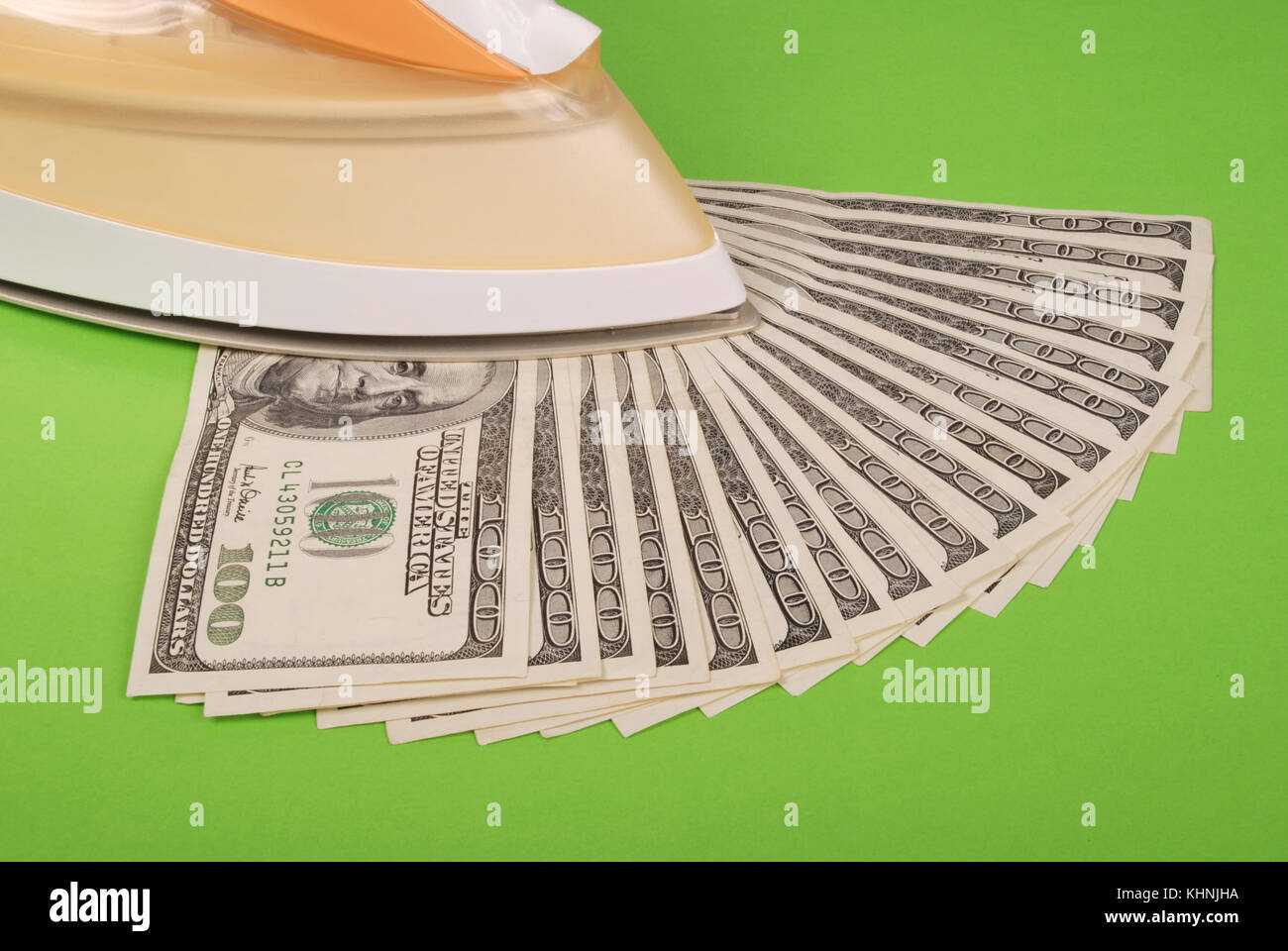 Dollars lay under an electric iron. On green background Stock Photo