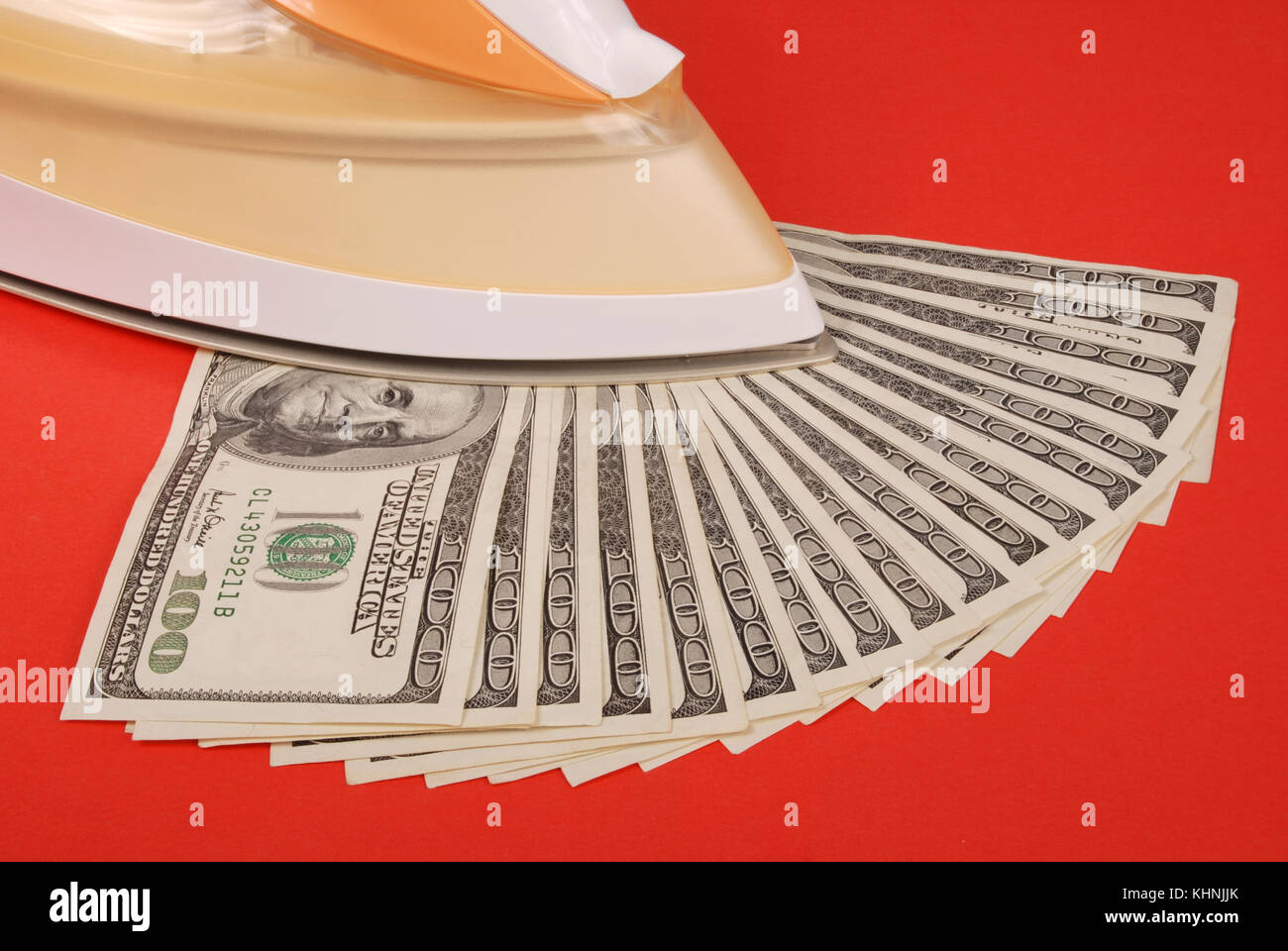 Dollars lay under an electric iron. On red background Stock Photo