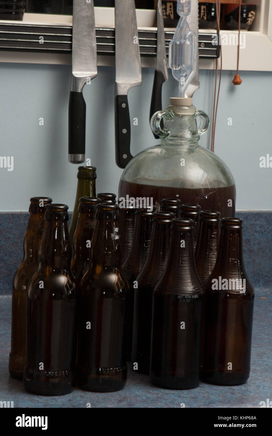 Fermented beer in a demijohn with airlock and dark brown bottles and over kitchen background Stock Photo