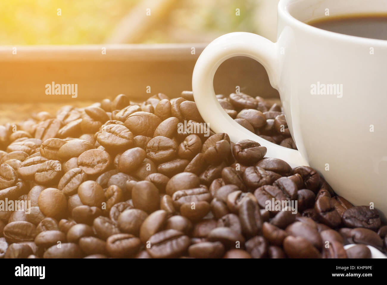 Coffee beans with white coffee mug blur background and light fair , A cup of hot coffee is placed beside the coffee beans with light fair Stock Photo