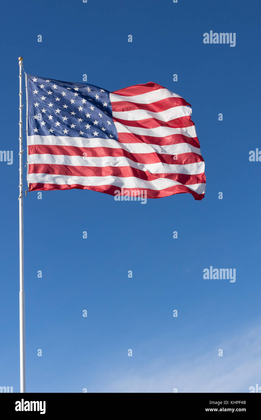 A red, white and blue American flag with stars and stripes unfurled in the wind. Photographed against a deep blue sky with cirrus clouds. Stock Photo