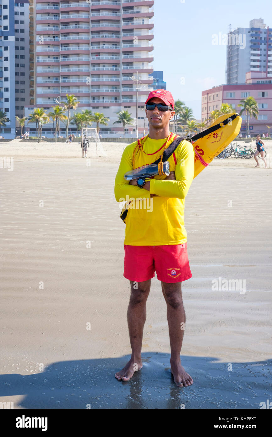 Male Brazilian firefighter lifeguard wearing a yellow shirt, red shorts, torpedo buoy standing on watch, Praia Grande Beach, state of Sao Paulo, Brazil. Stock Photo