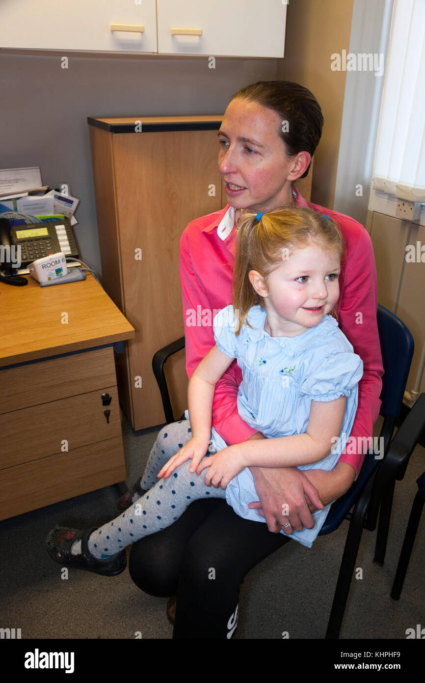 Mother / mum and three year old child / 3 yr old in a doctor's surgery talking to a doctor or practice nurse during an appointment at a medical centre Stock Photo