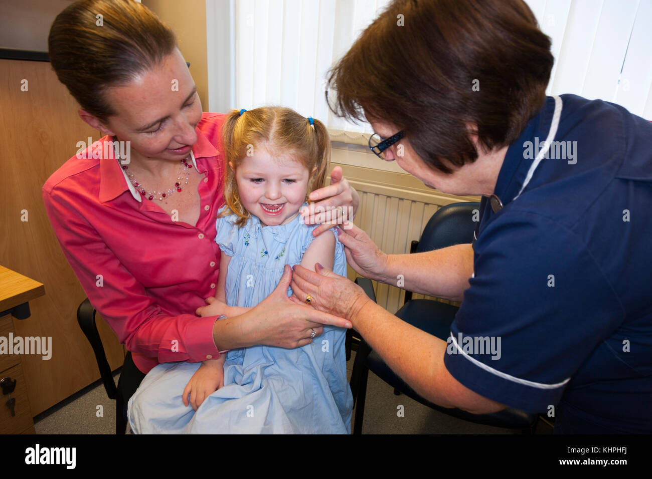 Practice nurse giving NHS 4-in-1 pre-school booster / Pre school booster & MMR second dose immunisation / inoculation / jab to 3 three year old child Stock Photo