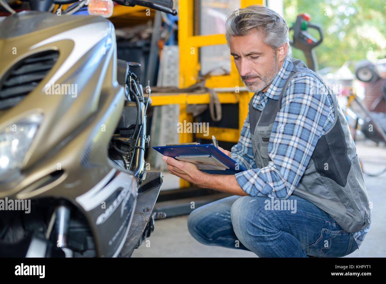 Mechanic crouched beside scooter holding clipboard Stock Photo