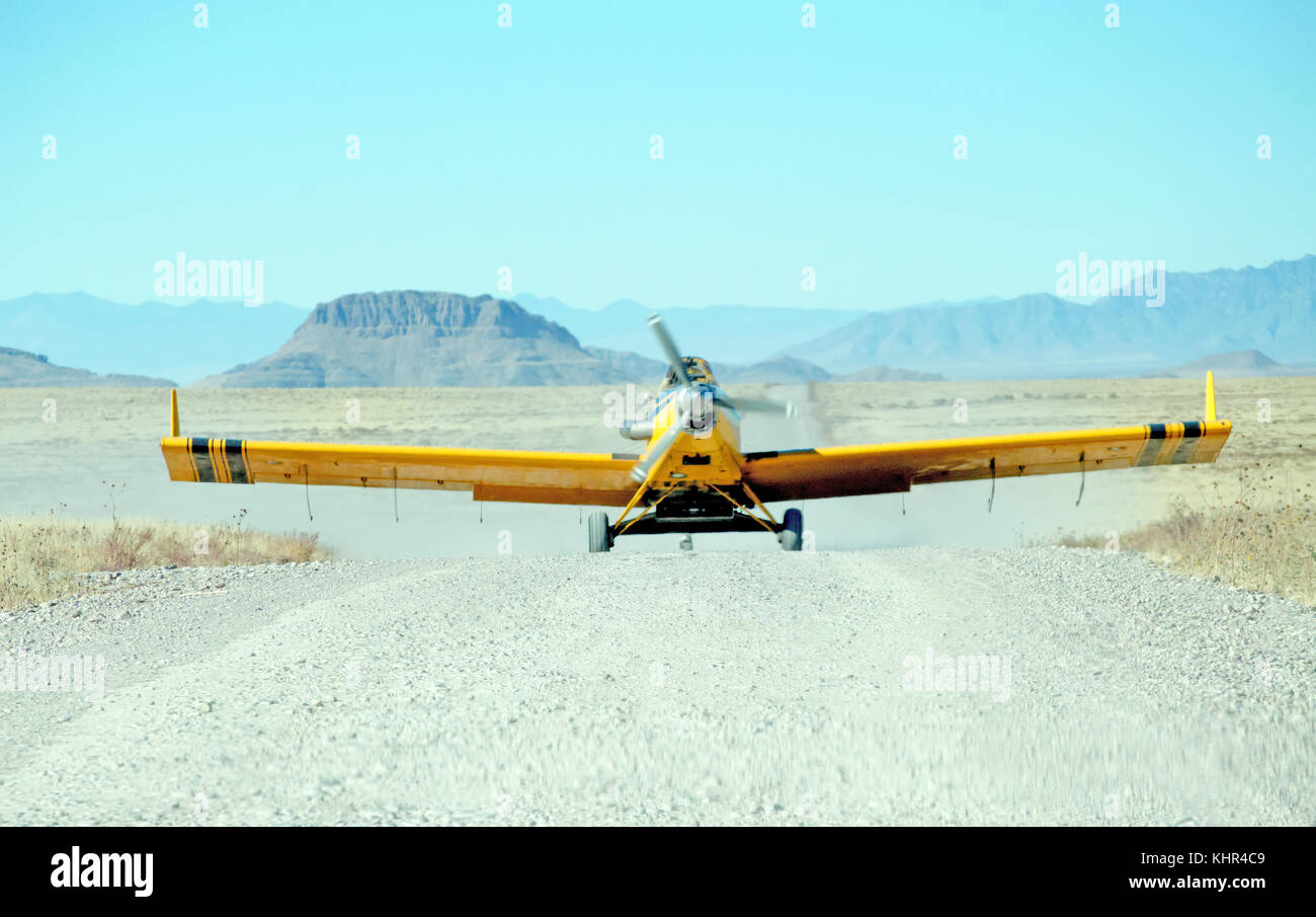 A yellow propeller driven seeder plane taking off of a desert road. Stock Photo