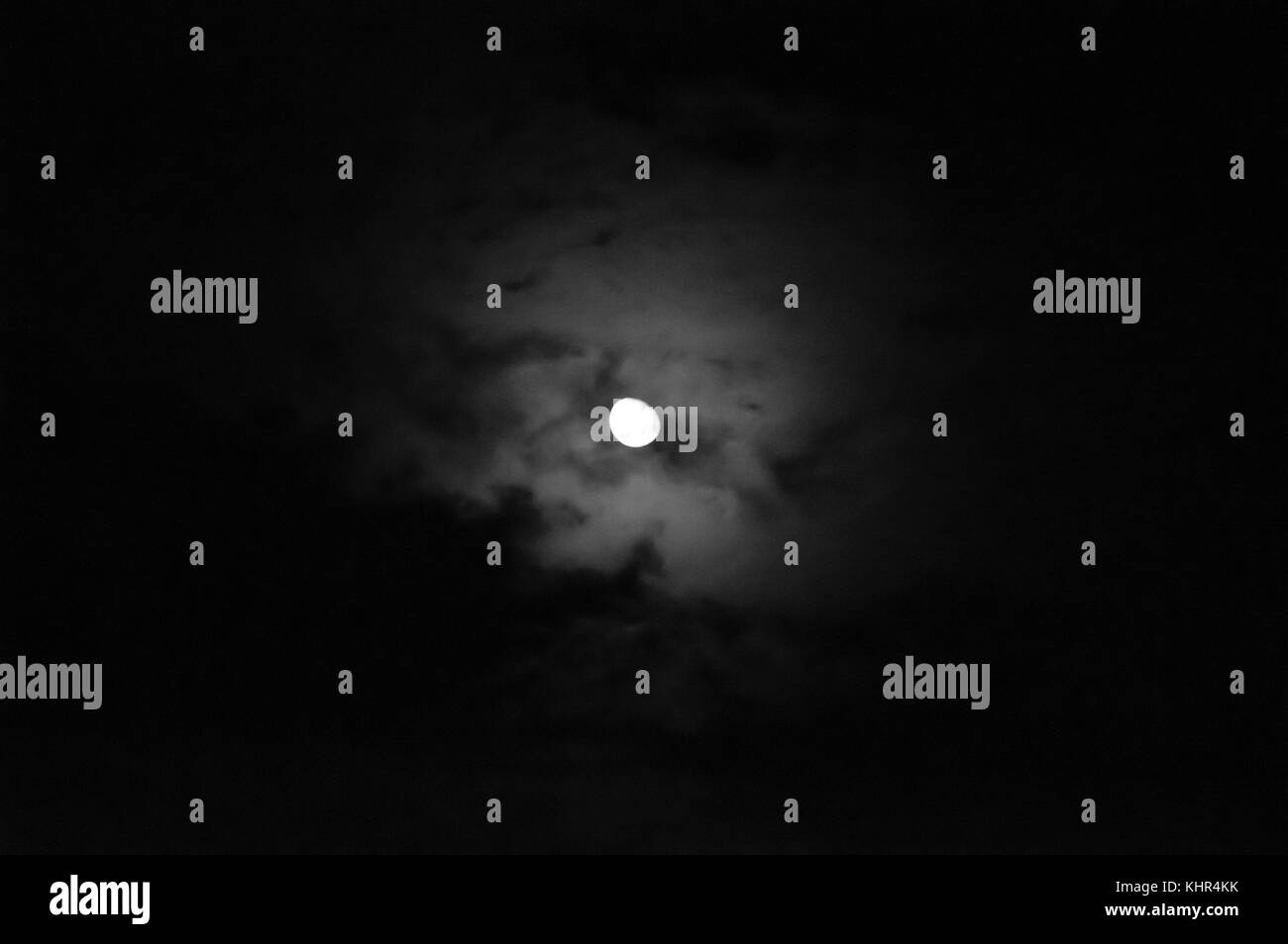 The moon peaking out from behind a cloudscape at night in black and white. Stock Photo