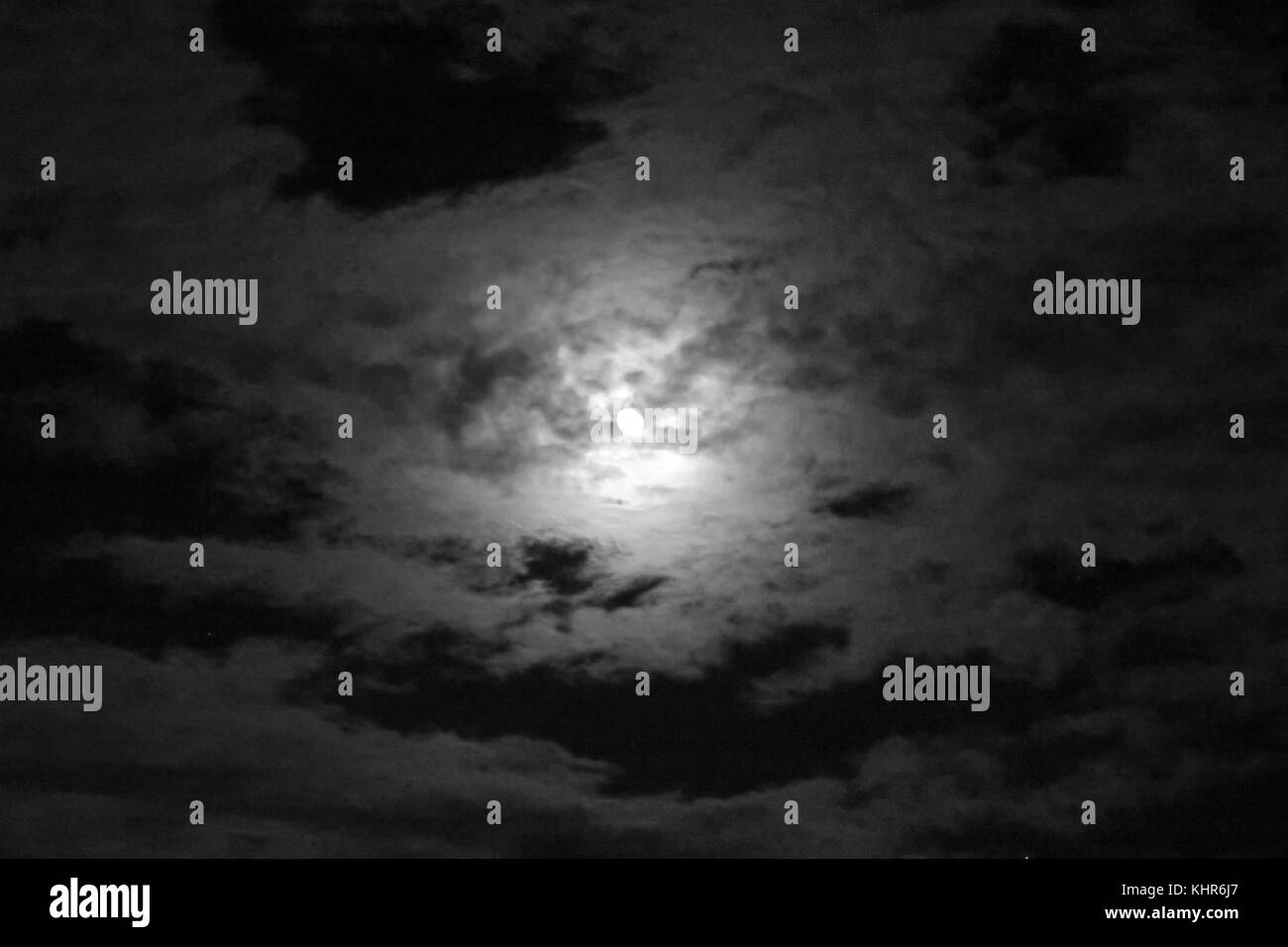 The moon peaking out from behind a cloudscape at night in black and white. Stock Photo