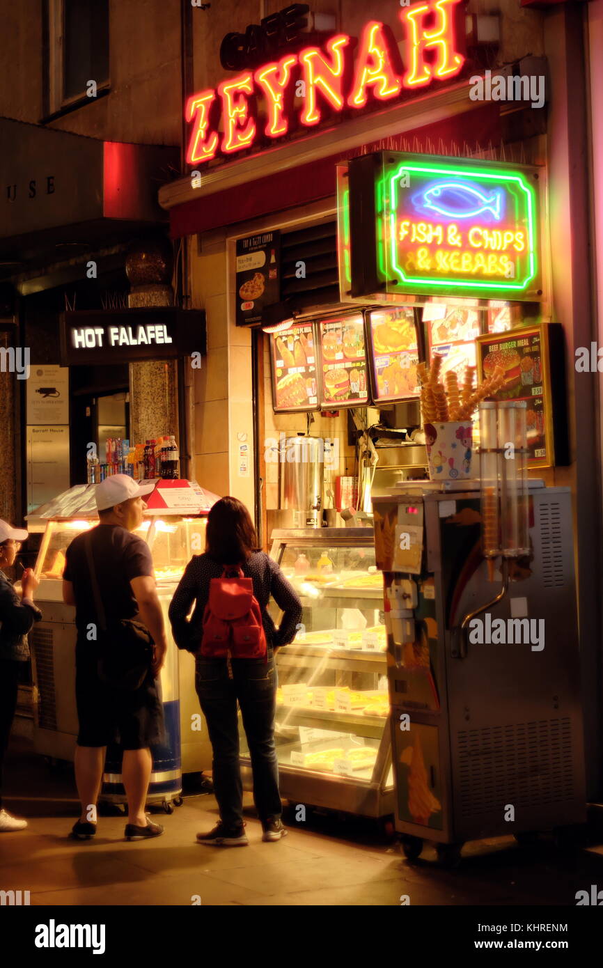 Tourist couple stand by ZEYNAH Fish & Chips & Kebab shops on Oxford Street, London, England Stock Photo