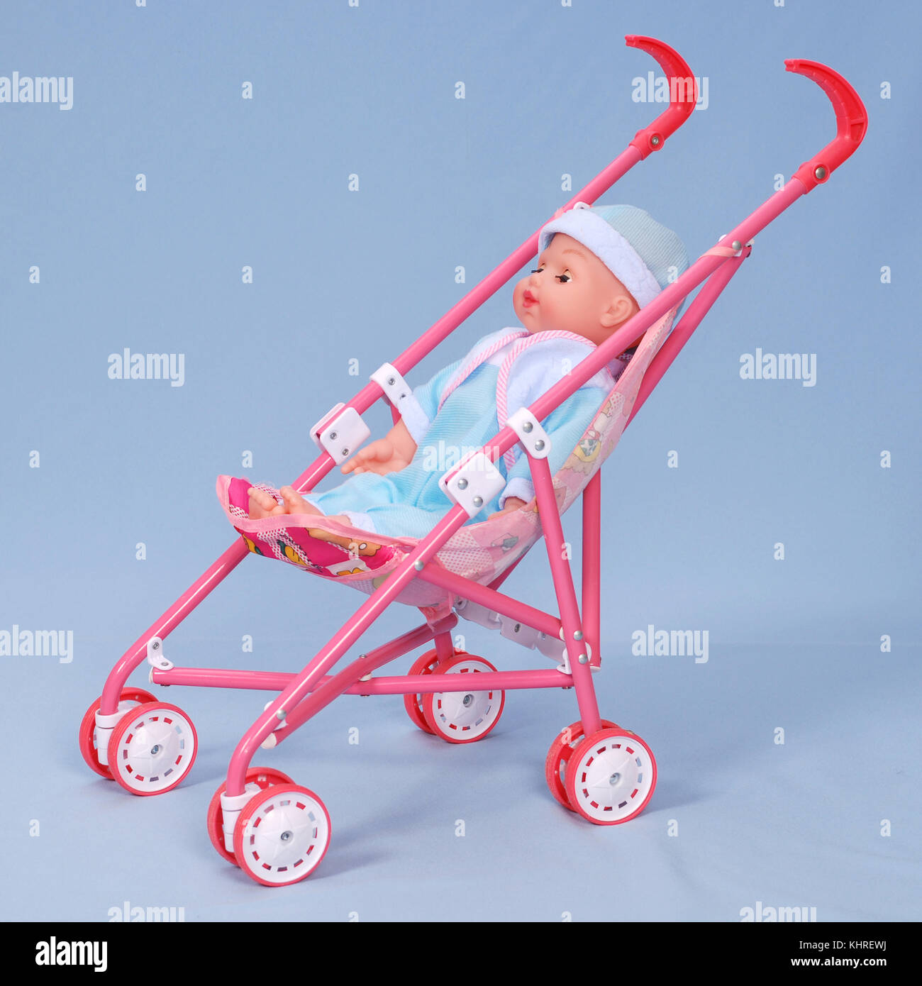 Toy baby buggy on blue background. On a carriage the doll lays Stock