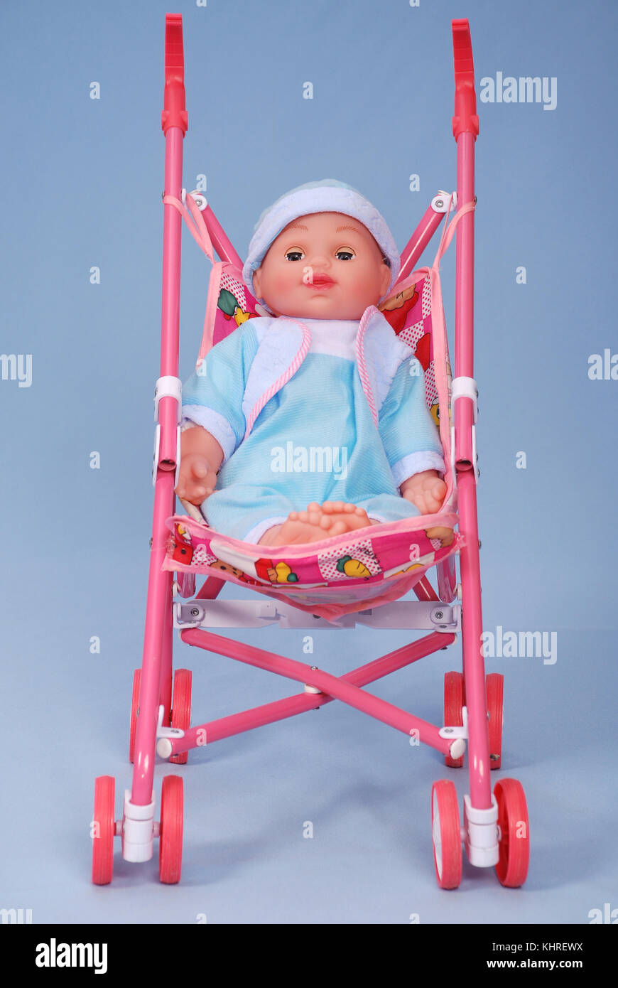 Toy baby buggy on blue background. On a carriage the doll lays Stock