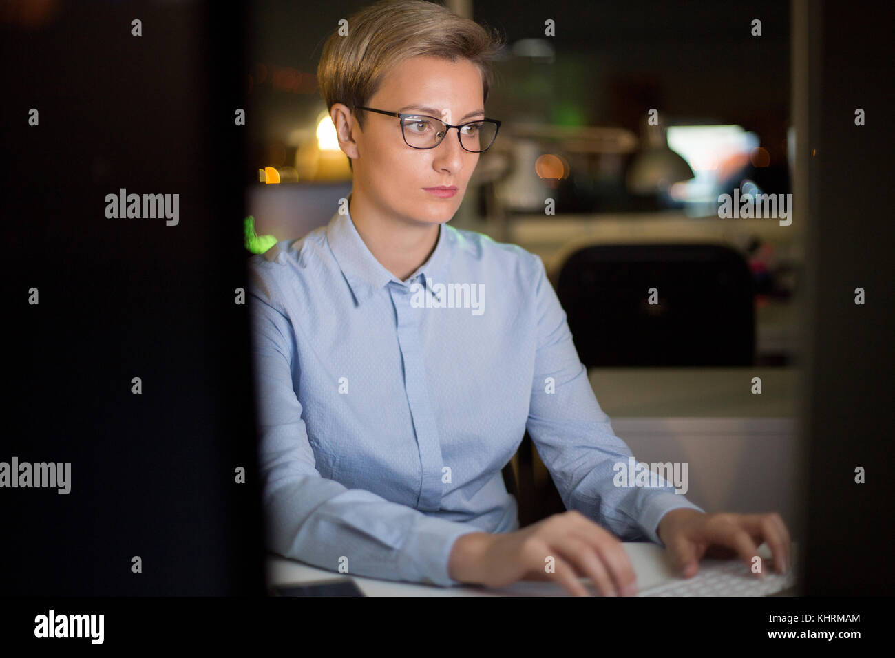 Waist-up portrait of concentrated middle-aged manager in eyeglasses sitting at office desk and analyzing results of accomplished work with help of com Stock Photo