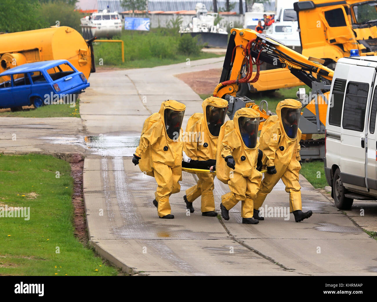 A group of four rescuers in the protective  clothing carry a stretcher with wounded after a industrial accident Stock Photo