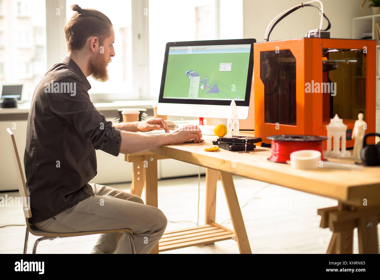 Profile view of confident bearded designer using computer program in order to create prototype with help of 3D printer, interior of modern studio on b Stock Photo