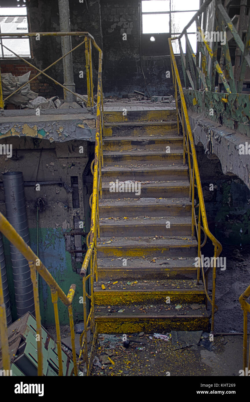 Stairway with yellow railing in a ruined industrial interior. Forgotten old factory. Stock Photo