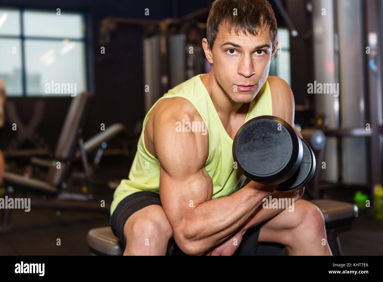 Man Straining As He Rows Young muscular man in a vest doing one-arm dumbbell rows on bench in ...